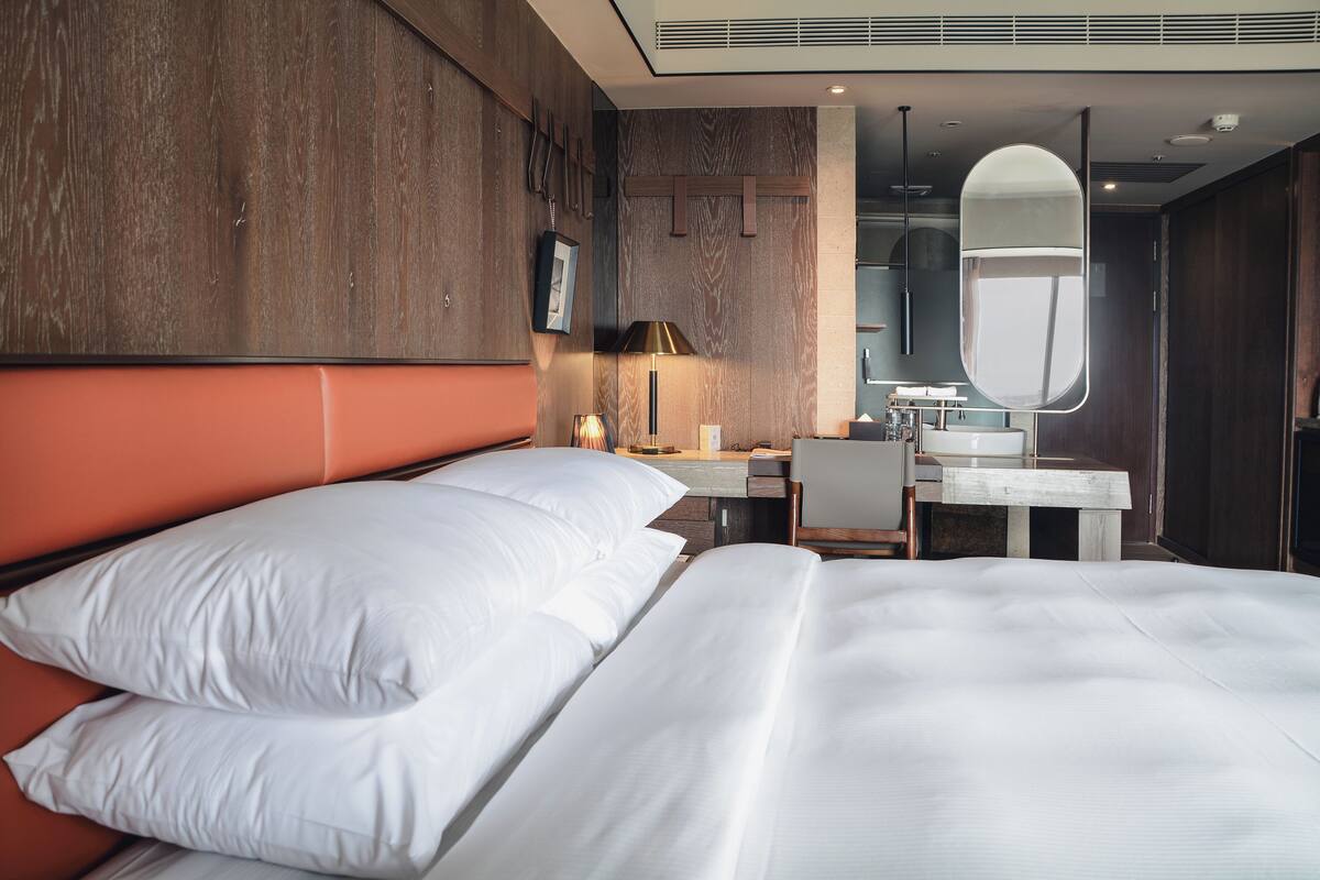 Ein Hotelzimmer mit einem großen Bett, einem Schreibtisch, einem Stuhl, einem Spiegel und einem Badezimmer mit Waschbecken und Spiegel.