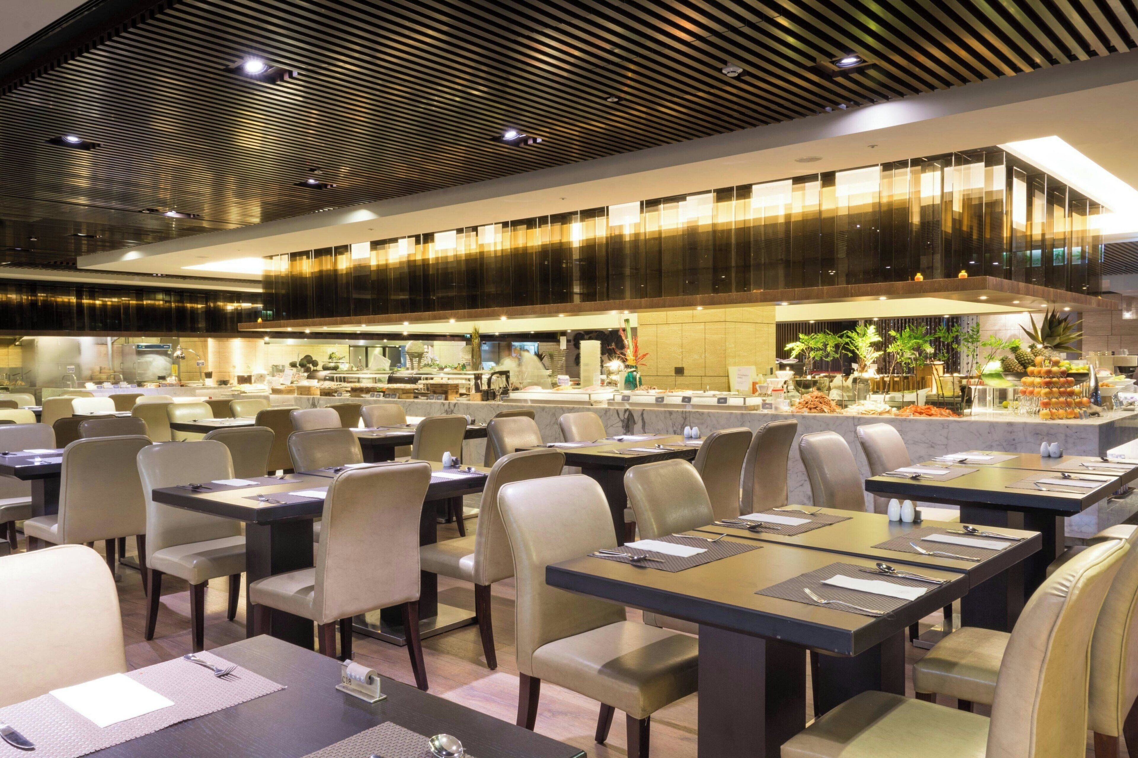 A modern restaurant with multiple dining tables and chairs, a kitchen area in the background, and a ceiling with a unique pattern.