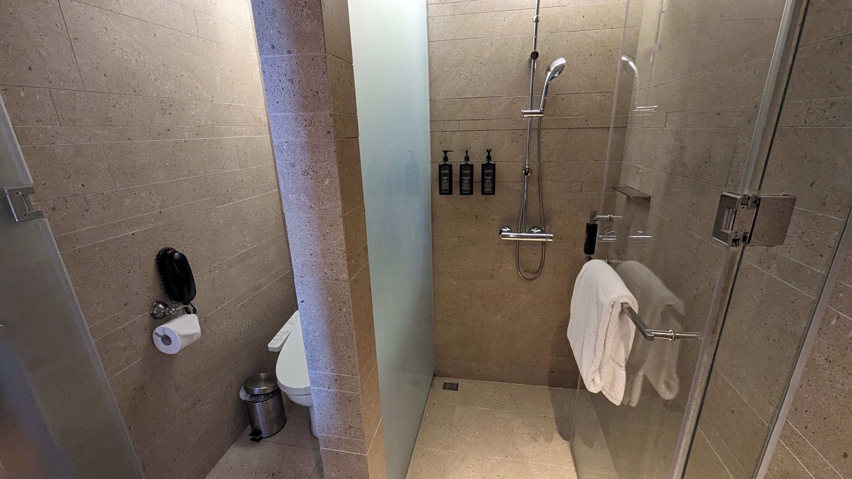 A modern bathroom with a glass shower enclosure, a toilet, a trash bin, and a towel rack.