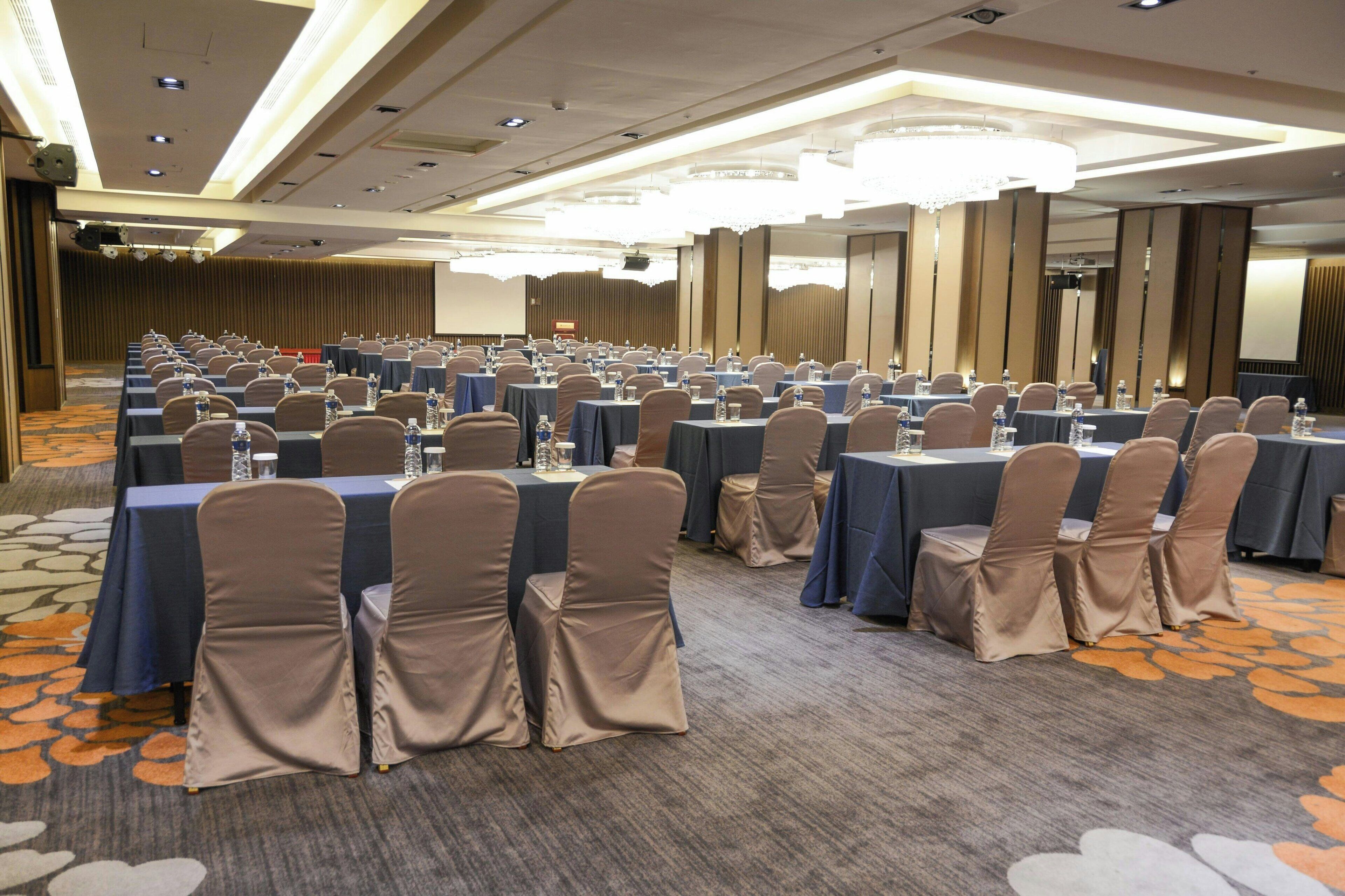 Un salón de conferencias con filas de mesas y sillas, equipado con botellas de agua y vasos.