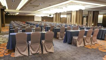 Un salón de conferencias con filas de mesas y sillas, equipado con botellas de agua y vasos.