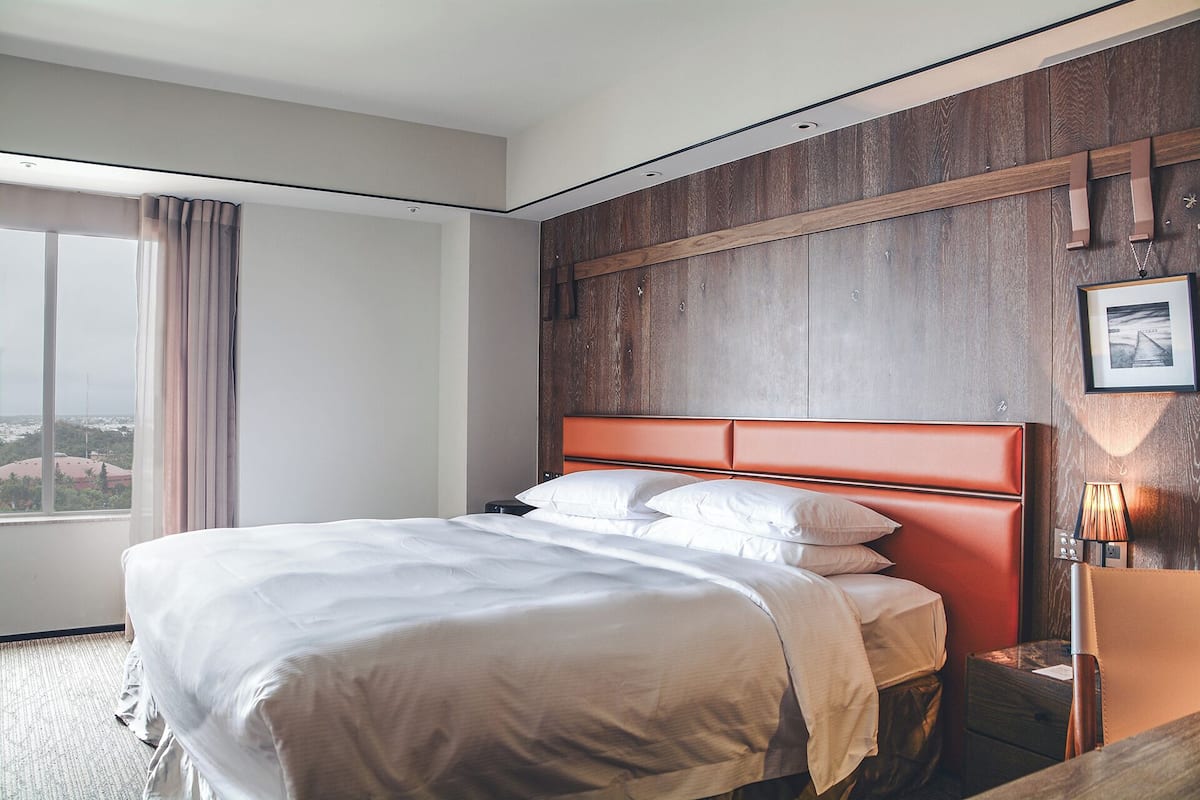 Ein Hotelzimmer mit einem großen Bett, einem Holz-Kopfteil, einem Nachttisch und einem Fenster mit Vorhängen.