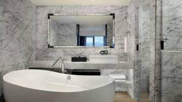 A modern bathroom with a large freestanding bathtub, a vanity with a mirror, and marble walls.