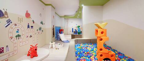 Zona de juegos infantiles con piscina de pelotas, tobogán y estructura para escalar.
