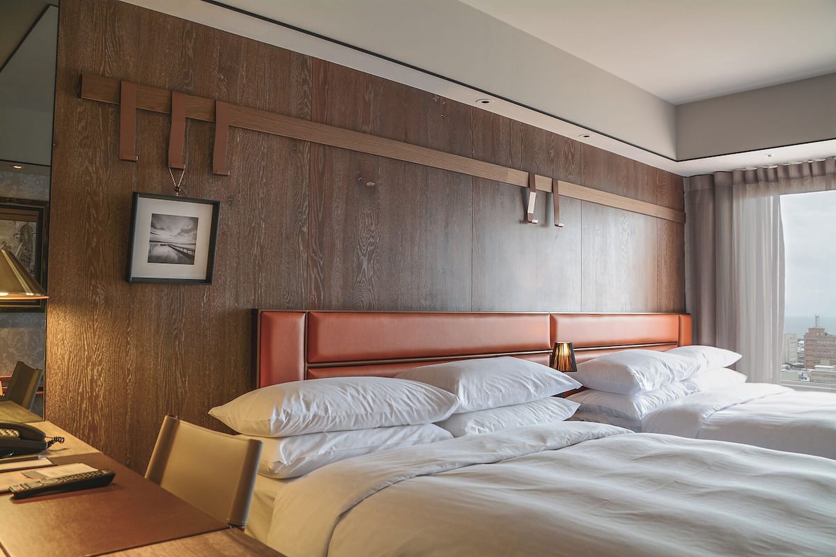 Ein Hotelzimmer mit einem großen Bett, einer Wand mit Holzvertäfelung, einem gerahmten Bild und Blick auf die Stadt.