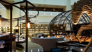 Un vestíbulo amplio con una zona de estar central, una gran escultura de madera y una biblioteca bien iluminada al fondo.