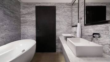 Un baño moderno con una bañera independiente, una puerta de madera oscura y una pared de mármol.