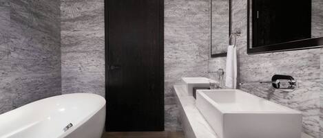 A modern bathroom with a freestanding bathtub, a dark wooden door, and a marble wall.