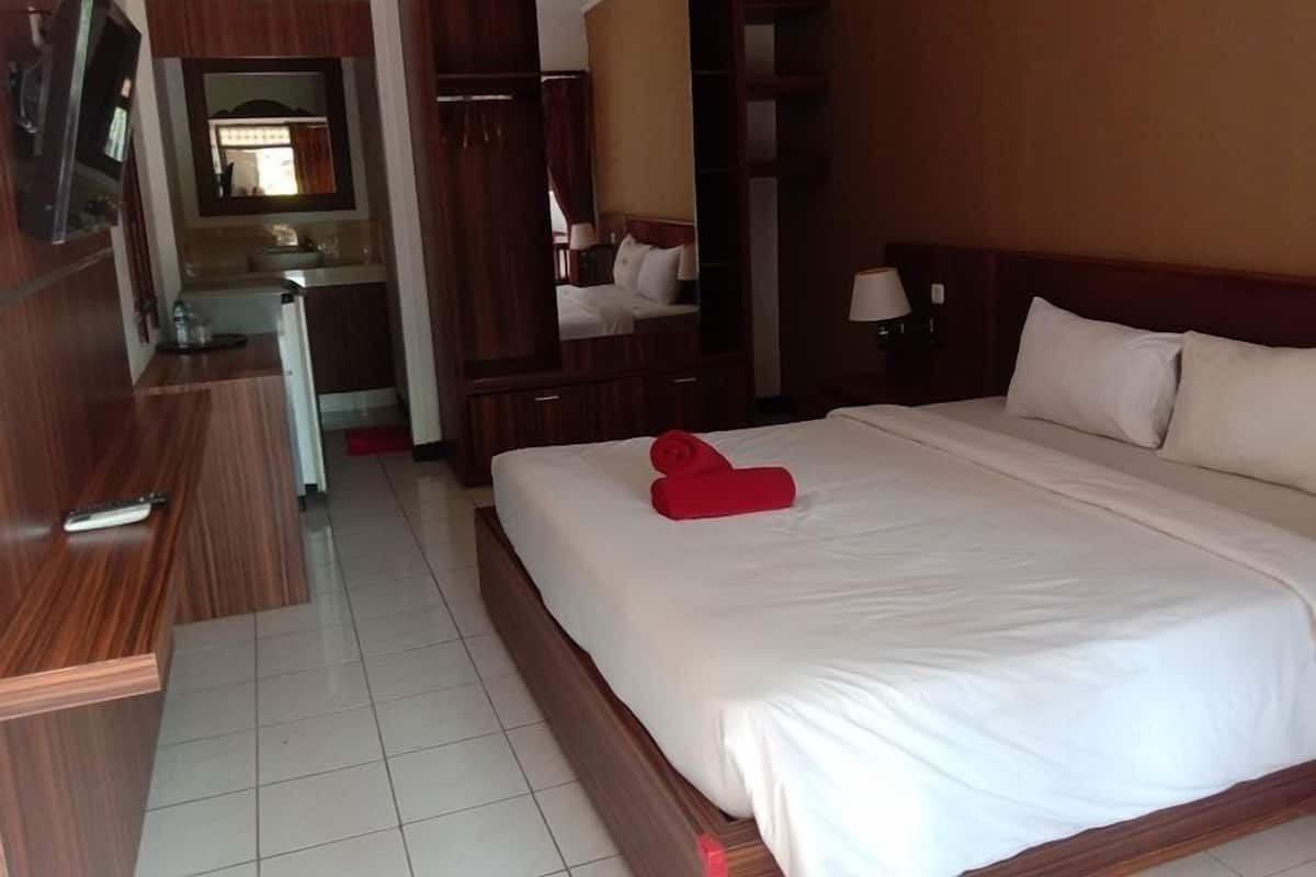 A hotel room with a large bed, a wooden wardrobe, a mirror, a desk, and a television.