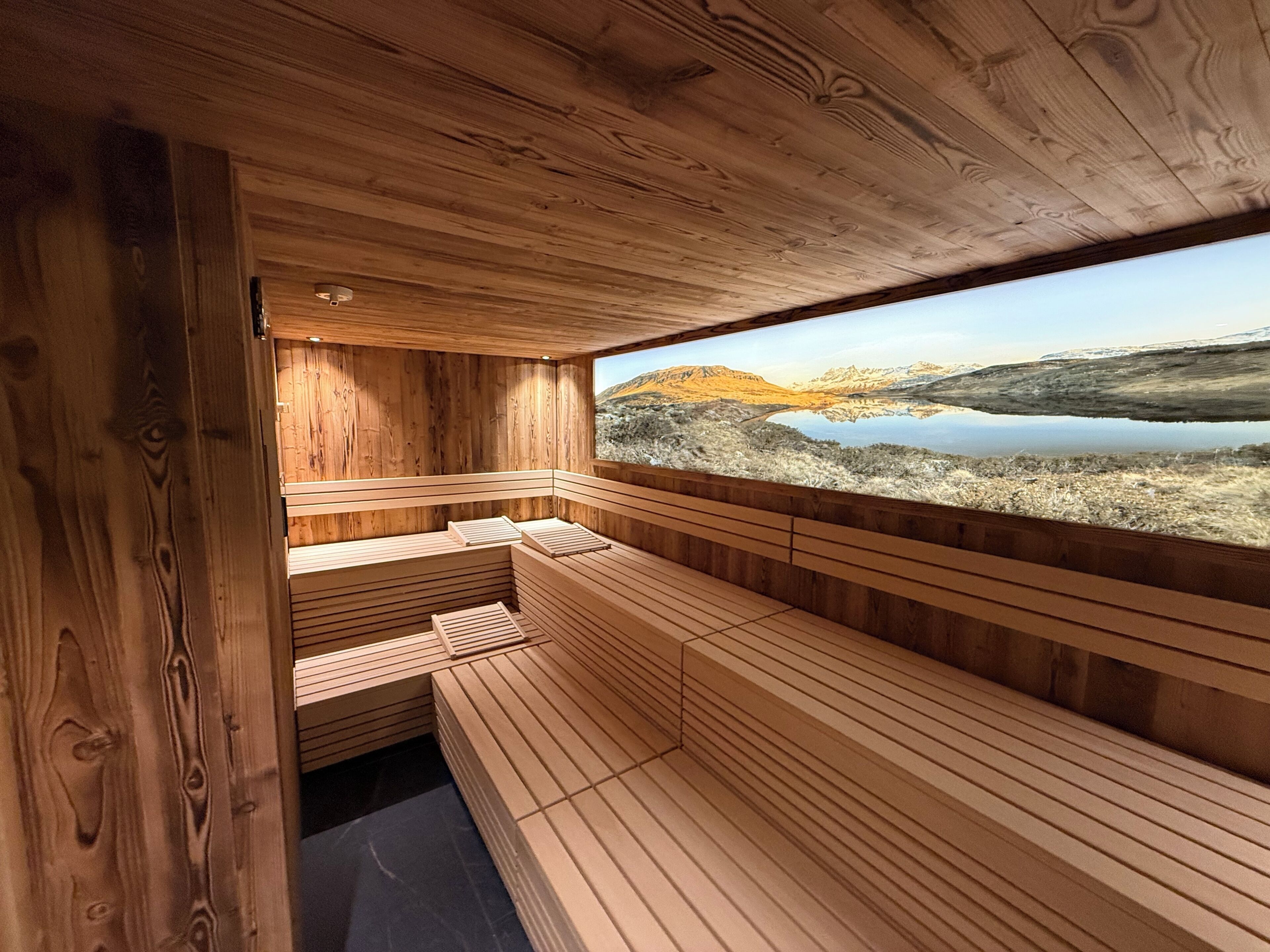 Una sauna de madera con bancos y vistas a un lago y montañas.