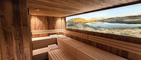 Una sauna de madera con bancos y vistas a un lago y montañas.
