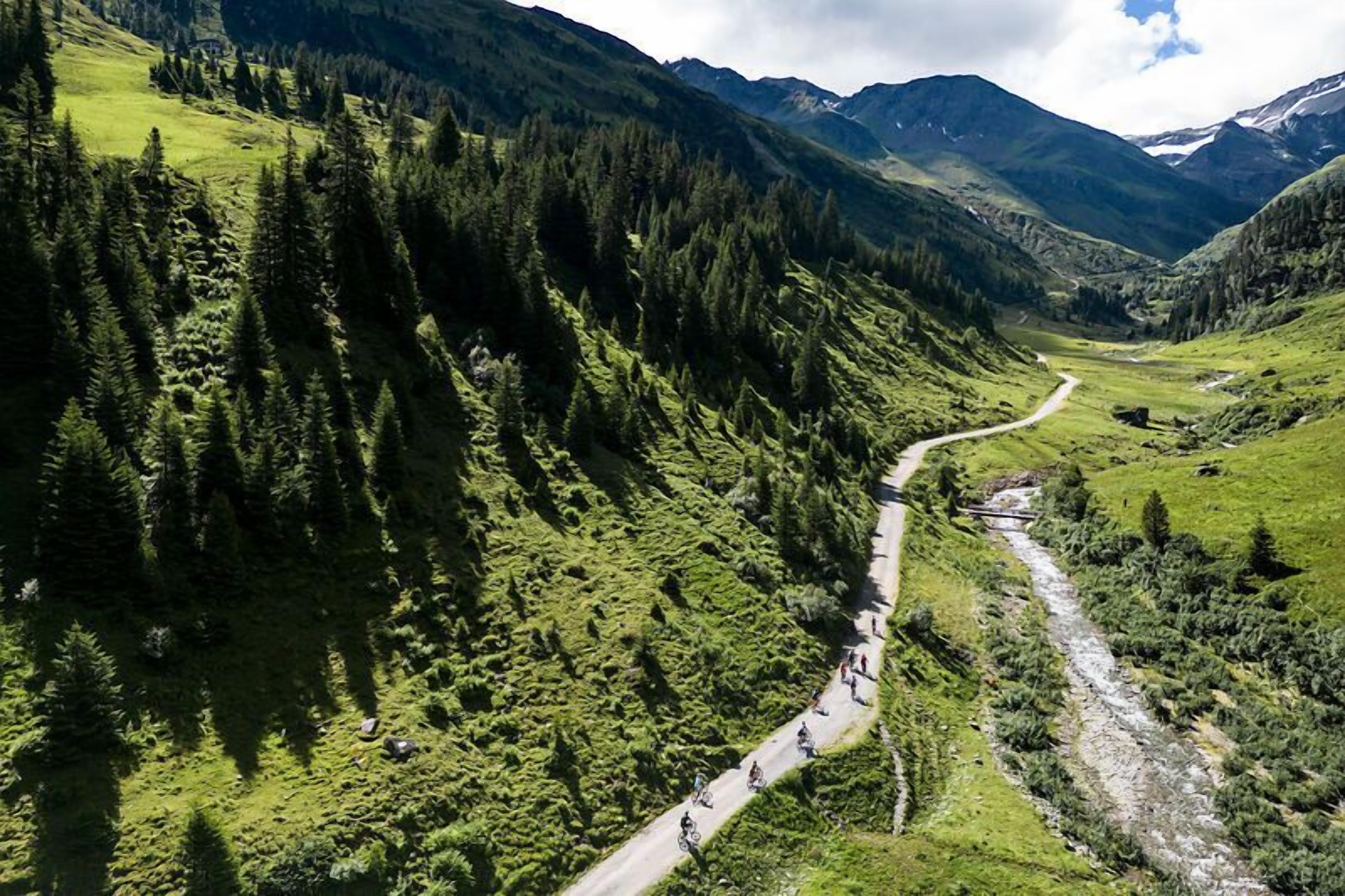 A mountain road winding through a valley with dense forests and a river.