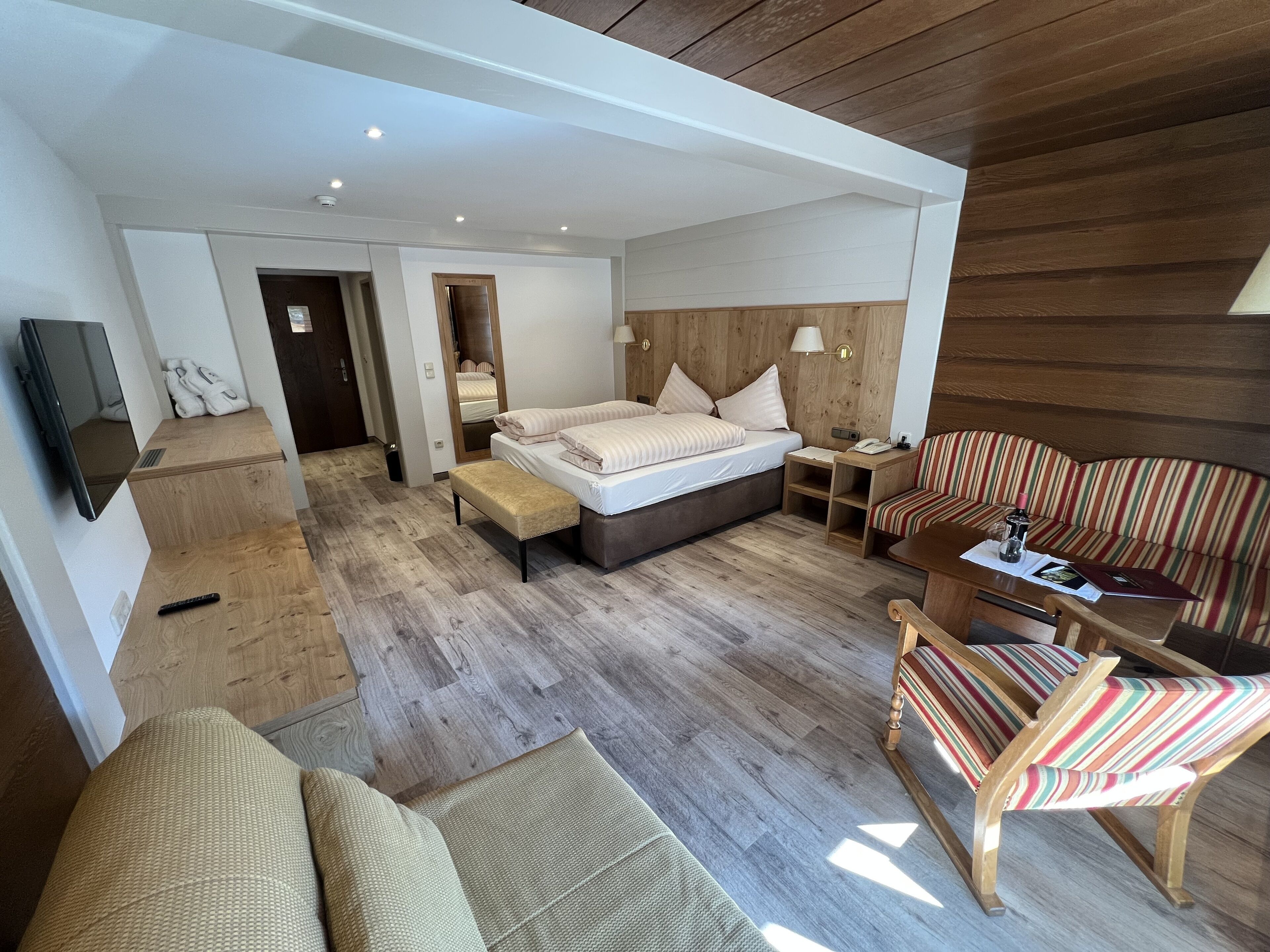 Una habitación de hotel moderna con cama, sofá, sillón, televisión y suelo de madera.