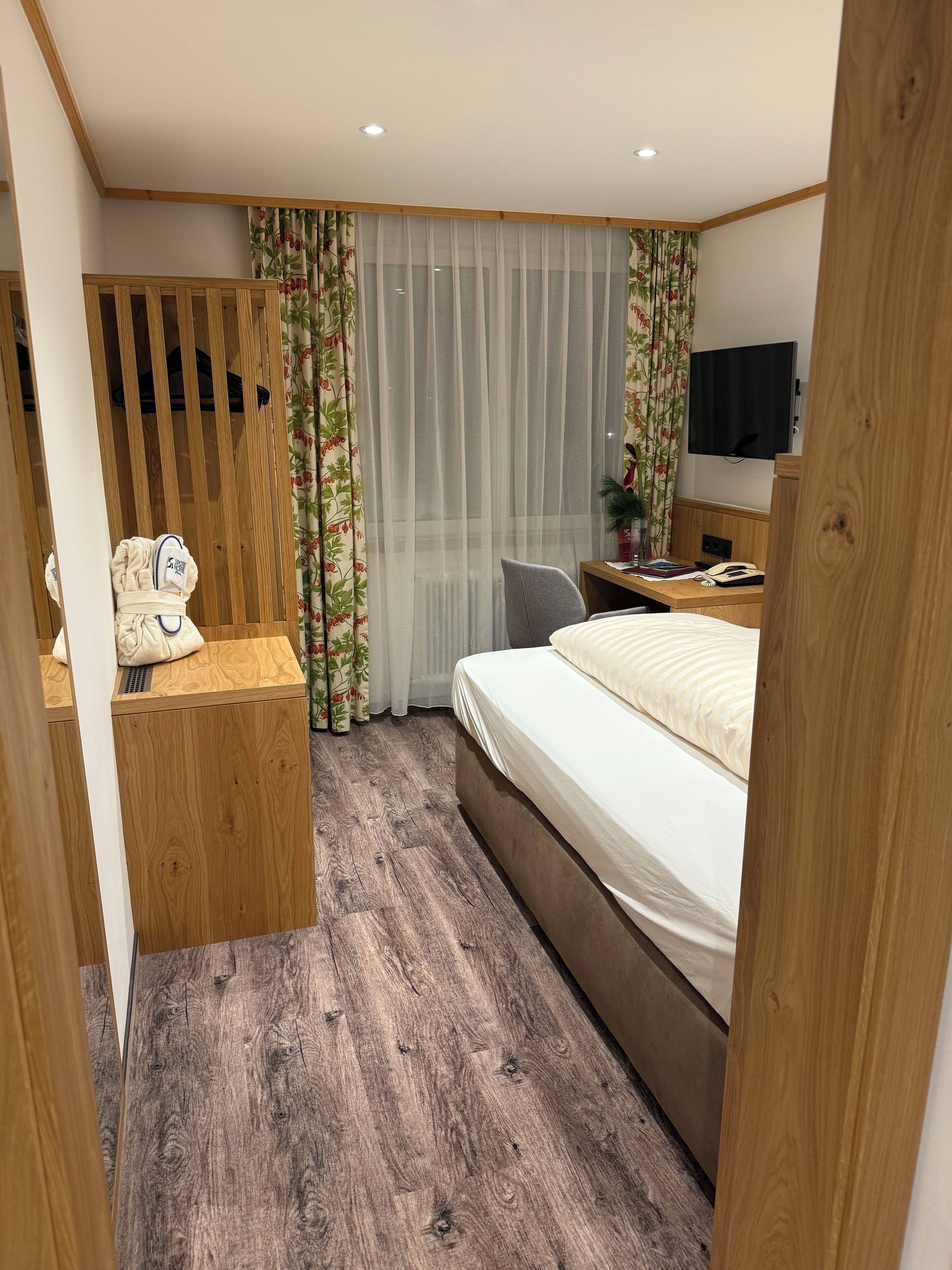 A modern hotel room with a wooden desk, a bed, a chair, and a television.