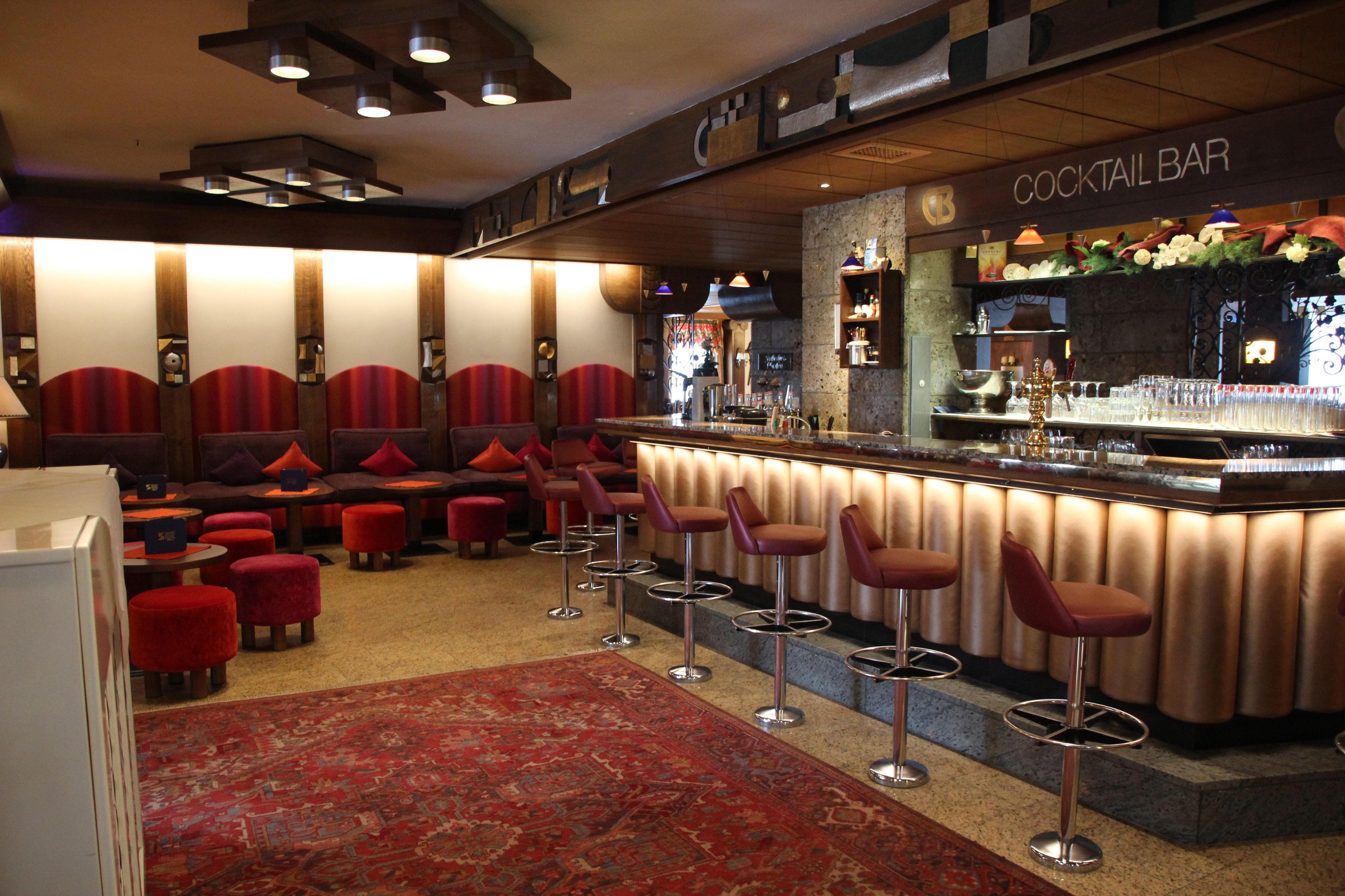 Eine Cocktailbar mit Barhocker, rotem Teppich und einem gemusterten Teppich.