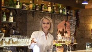 A bar area with a bartender, shelves with bottles, glasses, and a stone wall. - Sporthotel St. Anton (Sankt Anton am Arlberg)