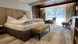 A spacious bedroom with a large bed, a bench, a desk, and a chair. - Sporthotel St. Anton (Sankt Anton am Arlberg)