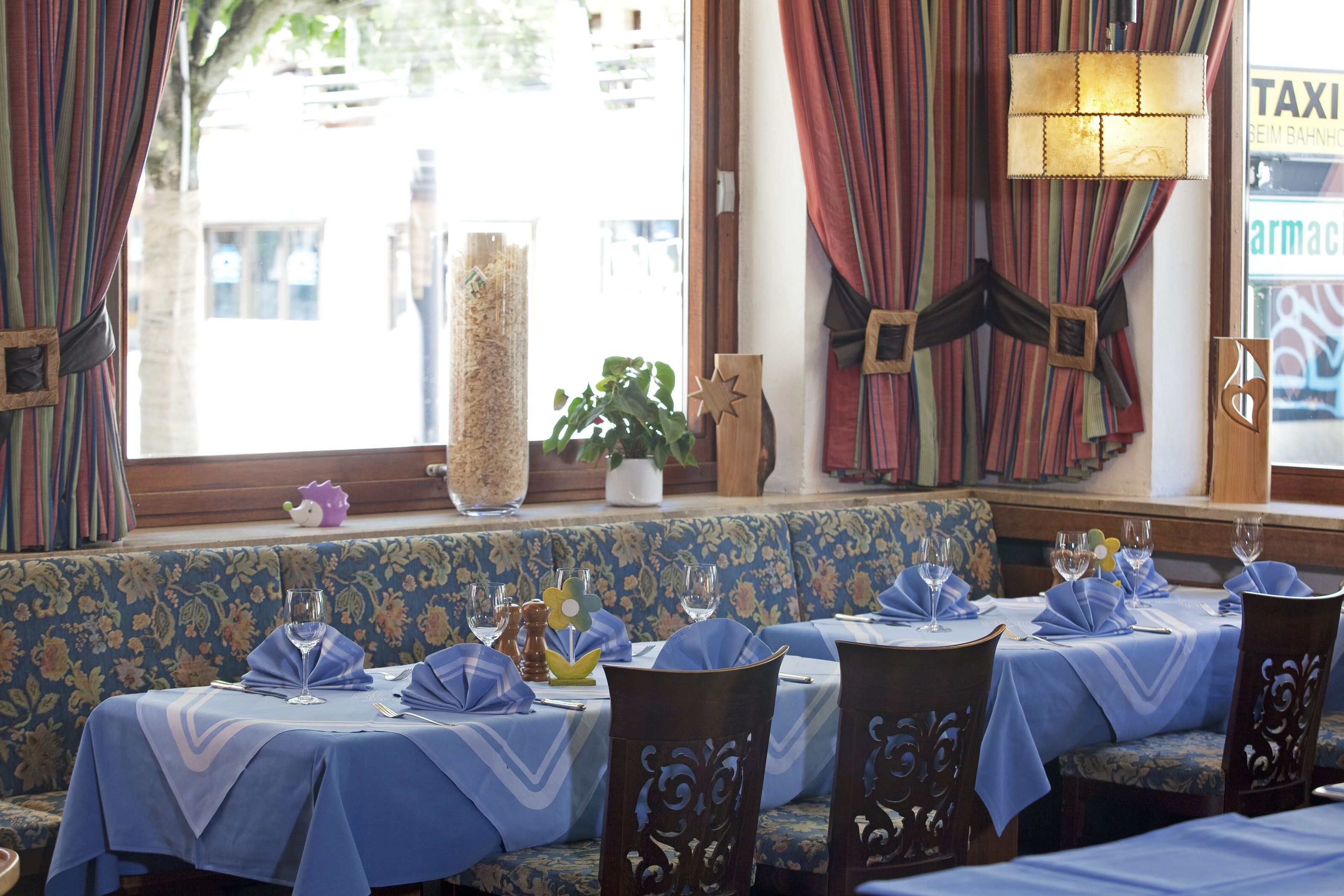 Interior de restaurante con cortinas azul y blanco a rayas, un sofá floral y mesas con manteles y servilletas azules.