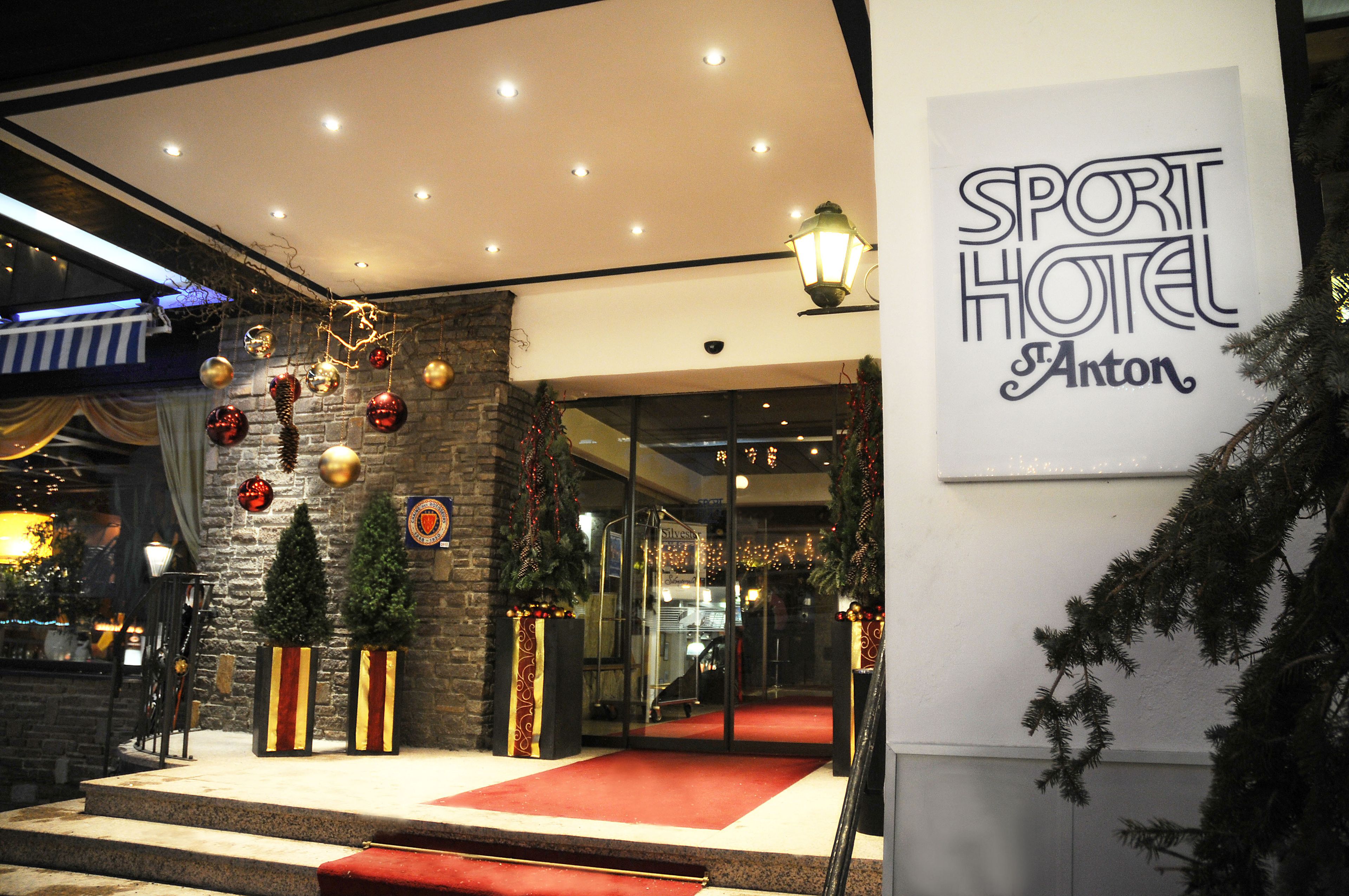 The entrance of Sport Hotel Anton with a red carpet, Christmas decorations, and a stone facade.