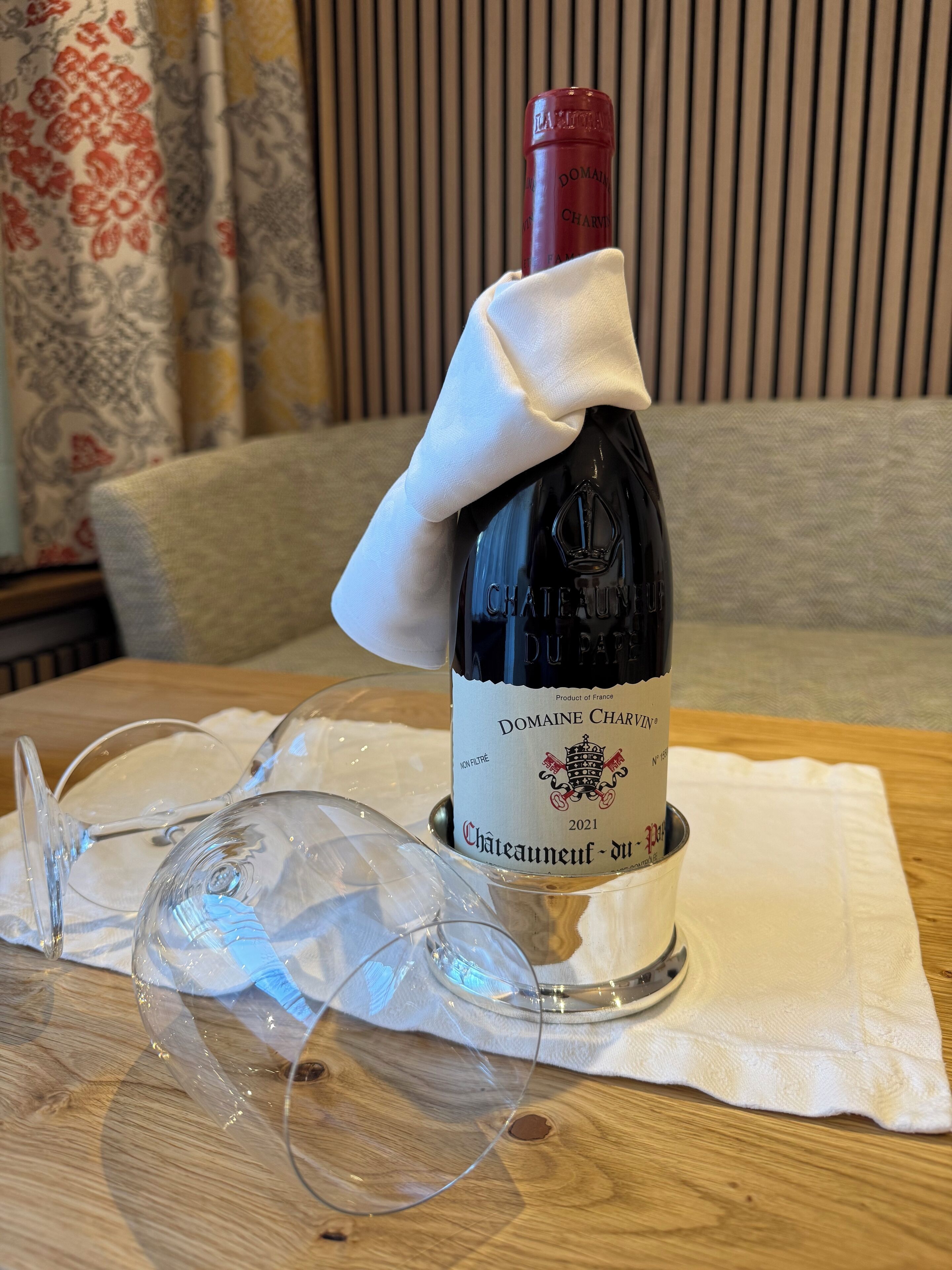 Una botella de vino Domaine Charvin sobre una mesa de madera con mantel blanco, acompañada por una copa de vino.