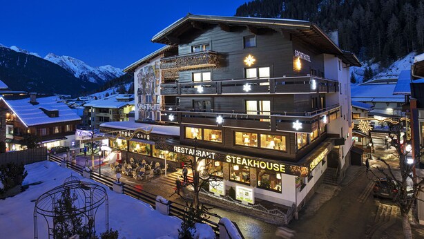 A multi-story hotel with a restaurant and steakhouse on the ground floor, surrounded by snow-covered mountains. - Sporthotel St. Anton (Sankt Anton am Arlberg)