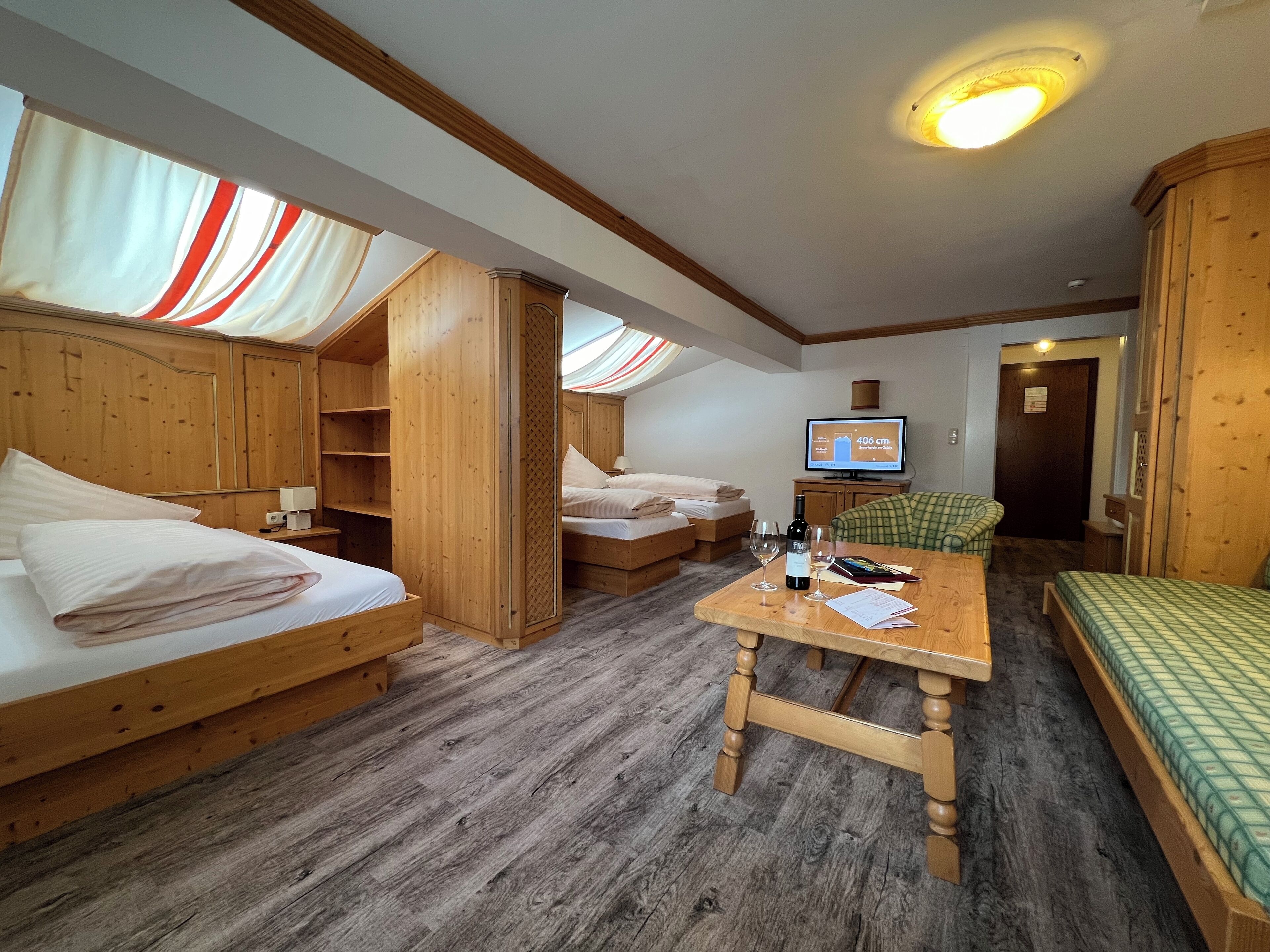 A cozy room with wooden furniture, including a bed, a sofa, and a table with a bottle and glasses.