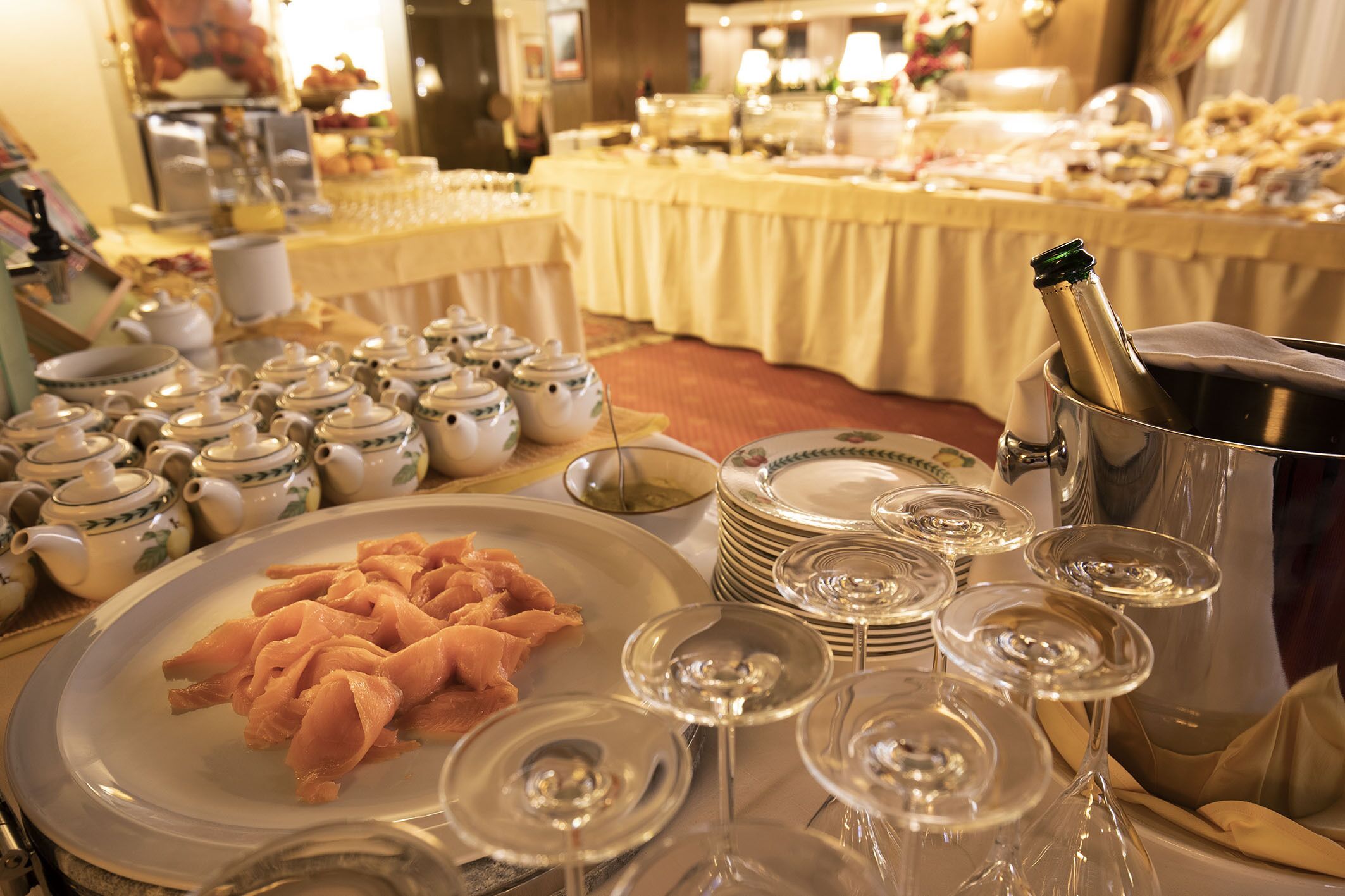 Een buffettafel met borden vol eten, wijn glazen en een champagnefles in een emmer.