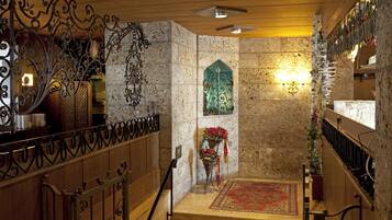 Stunning staircase with a decorative metal railing and intricate designs, leading to a landing area with a textured stone wall and a beautiful stained glass window.