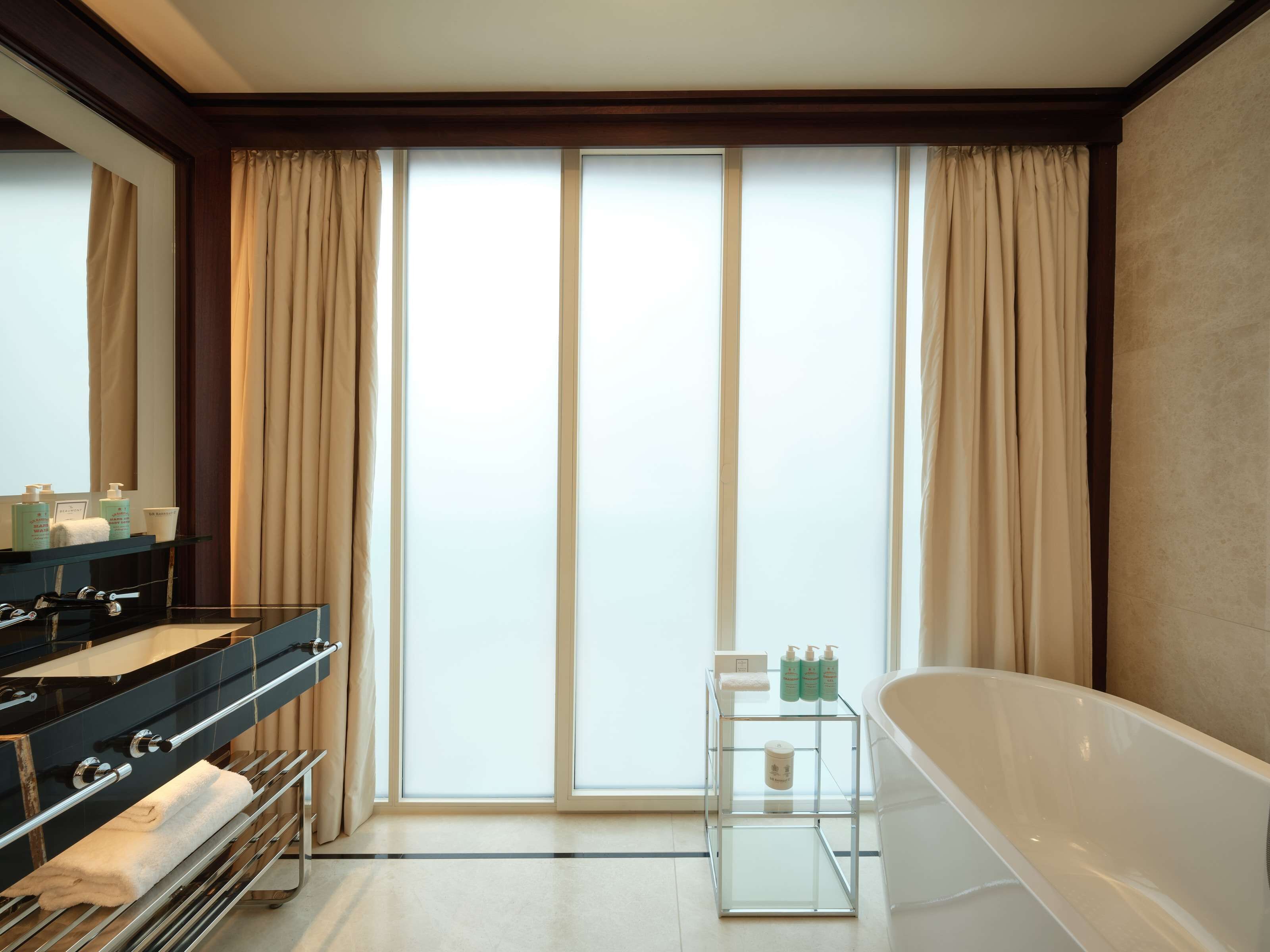 A modern bathroom with a large bathtub, a glass vanity with a black countertop, and a glass shelf with toiletries.