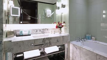 A modern bathroom with a large mirror, marble countertops, a bathtub, and a patterned floor.