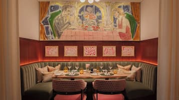 A dining area with a high-backed booth seating, a table set with glasses and cutlery, and a mural above the seating.