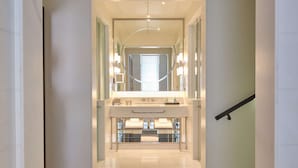 A modern, well-lit hallway leading to a bathroom with a large mirror, vanity, and a staircase. - The Beaumont Mayfair (London)