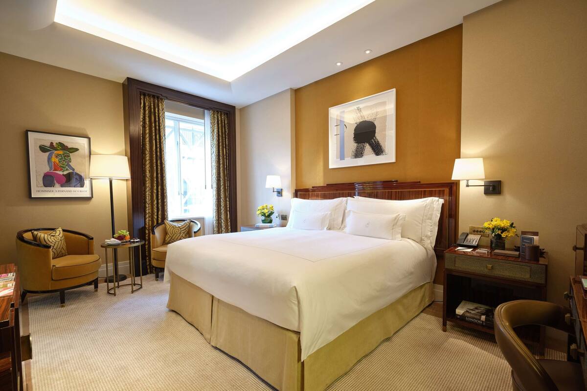 Ein Hotelzimmer mit einem großen Bett, einem Schreibtisch mit Lampe, einem Sessel und einem kleinen Tisch mit Blumen.