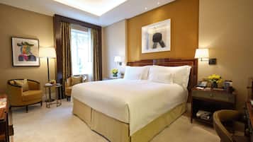 A hotel room with a large bed, a desk with a lamp, a chair, and a small table with flowers.