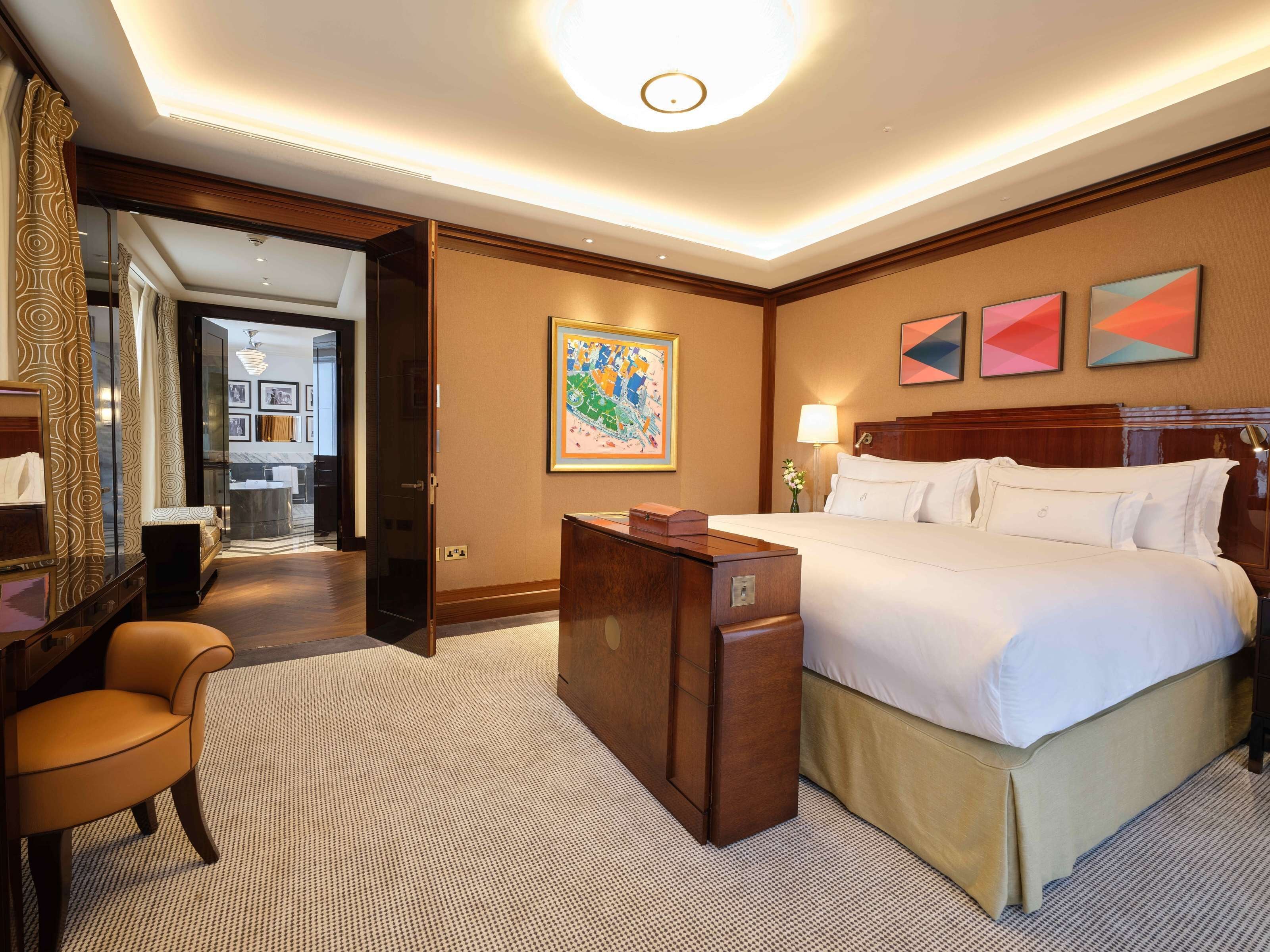 A hotel room with a bed, a desk, a chair, a mirror, and a bathroom visible through an open door.