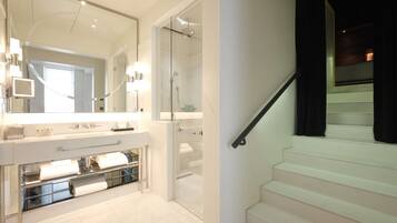 Un baño moderno con un espejo grande, cabina de ducha de vidrio y piso cubierto de baldosas blancas.