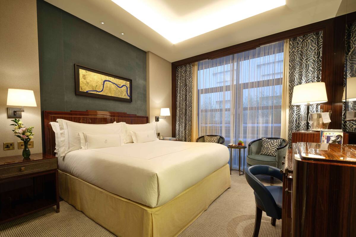 Ein Hotelzimmer mit einem großen Bett, zwei Nachttischen, einem Schreibtisch, einem Sessel und einem großen Fenster mit Vorhängen.