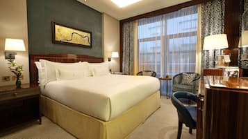 A hotel room with a large bed, two bedside tables, a desk, a chair, and a large window with curtains.