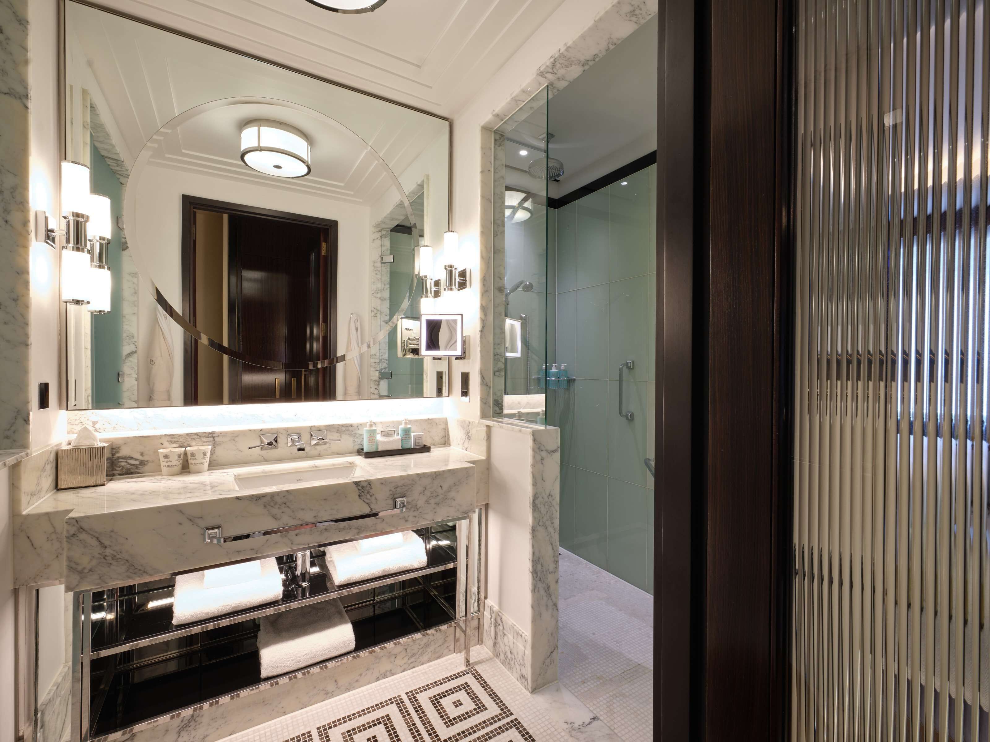 Une salle de bain moderne avec un grand miroir, des plans de travail en marbre et une cabine de douche en verre.