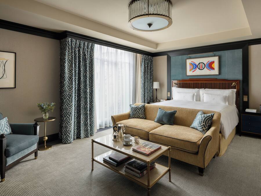 A hotel room with a bed, a sofa, a coffee table, and a desk with a lamp.