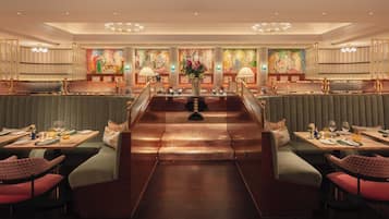 A spacious, elegantly designed restaurant with high-backed booths, a central staircase, and a large mural on the back wall.