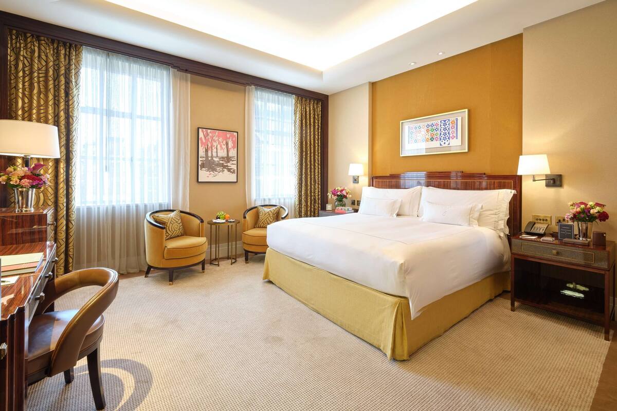 Ein Hotelzimmer mit einem großen Bett, zwei Sesseln, einem Schreibtisch und einem Nachttisch mit Lampe und Telefon.