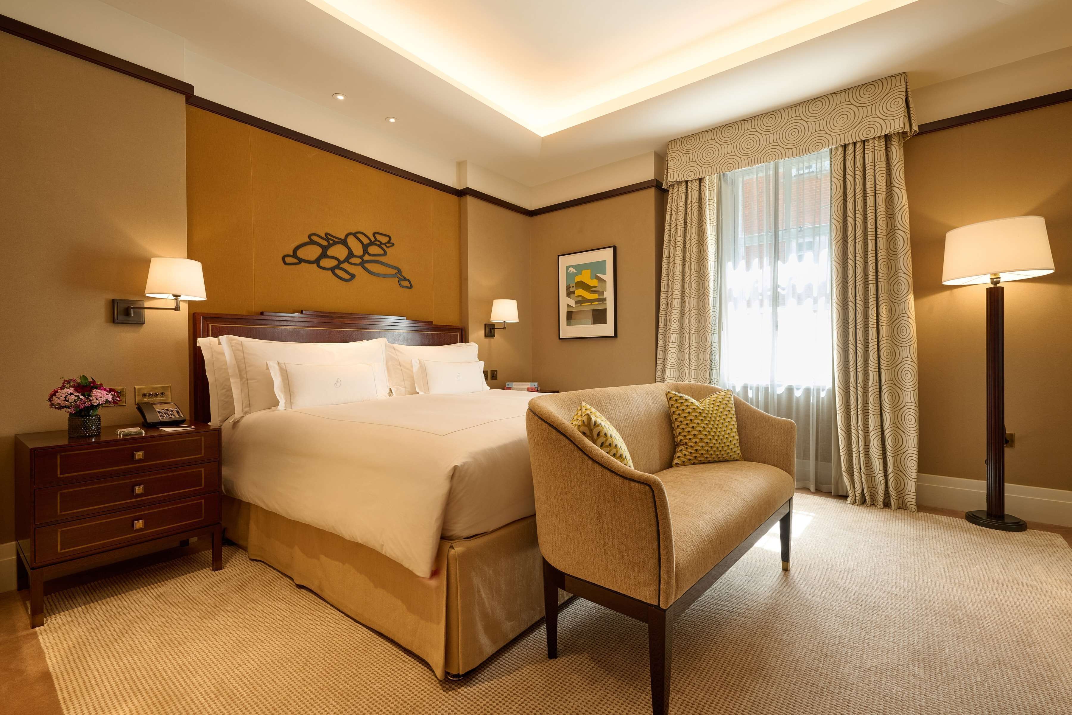 A hotel room with a large bed, a chair, a nightstand, and a lamp.