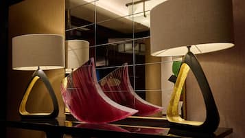 A modern hotel room with a large mirror reflecting the room's interior, including a unique red fabric sculpture and two contemporary lamps.