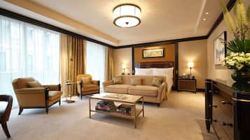 Une chambre d’hôtel avec un grand lit, un canapé, un fauteuil, une table basse avec des livres, une table de chevet et une lampe.