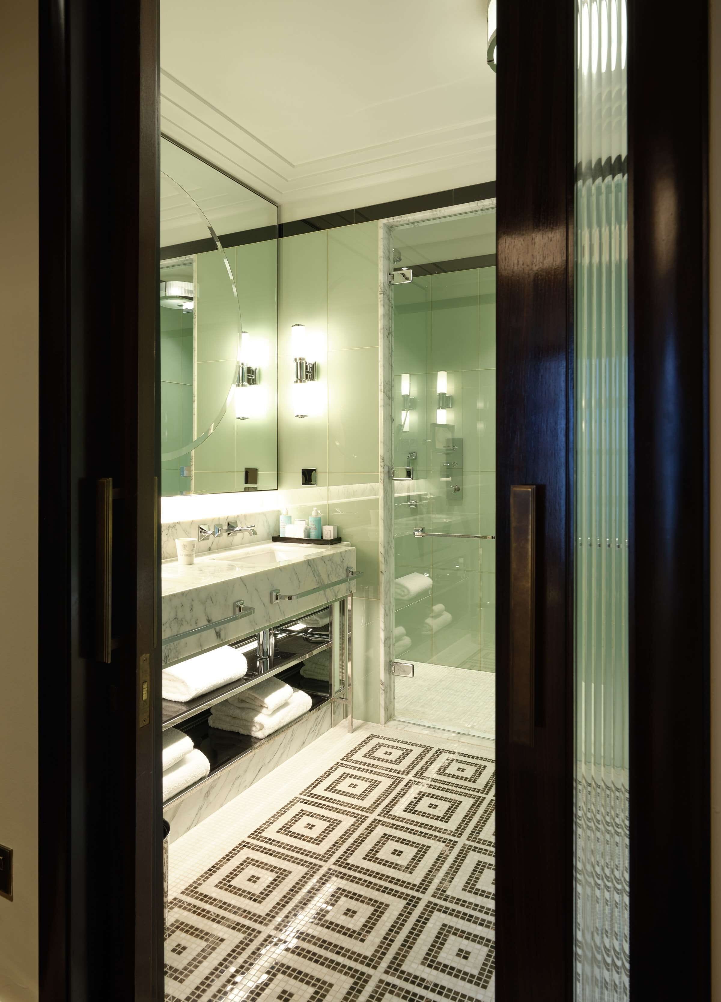 A modern bathroom with a glass shower enclosure, a marble vanity, and a patterned floor.