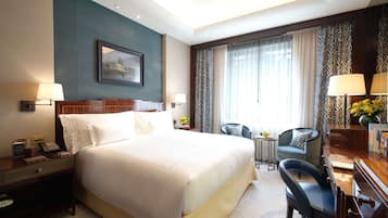 A hotel room with a large bed, bedside tables, a desk with a chair, a small table with a chair, and a window with curtains.