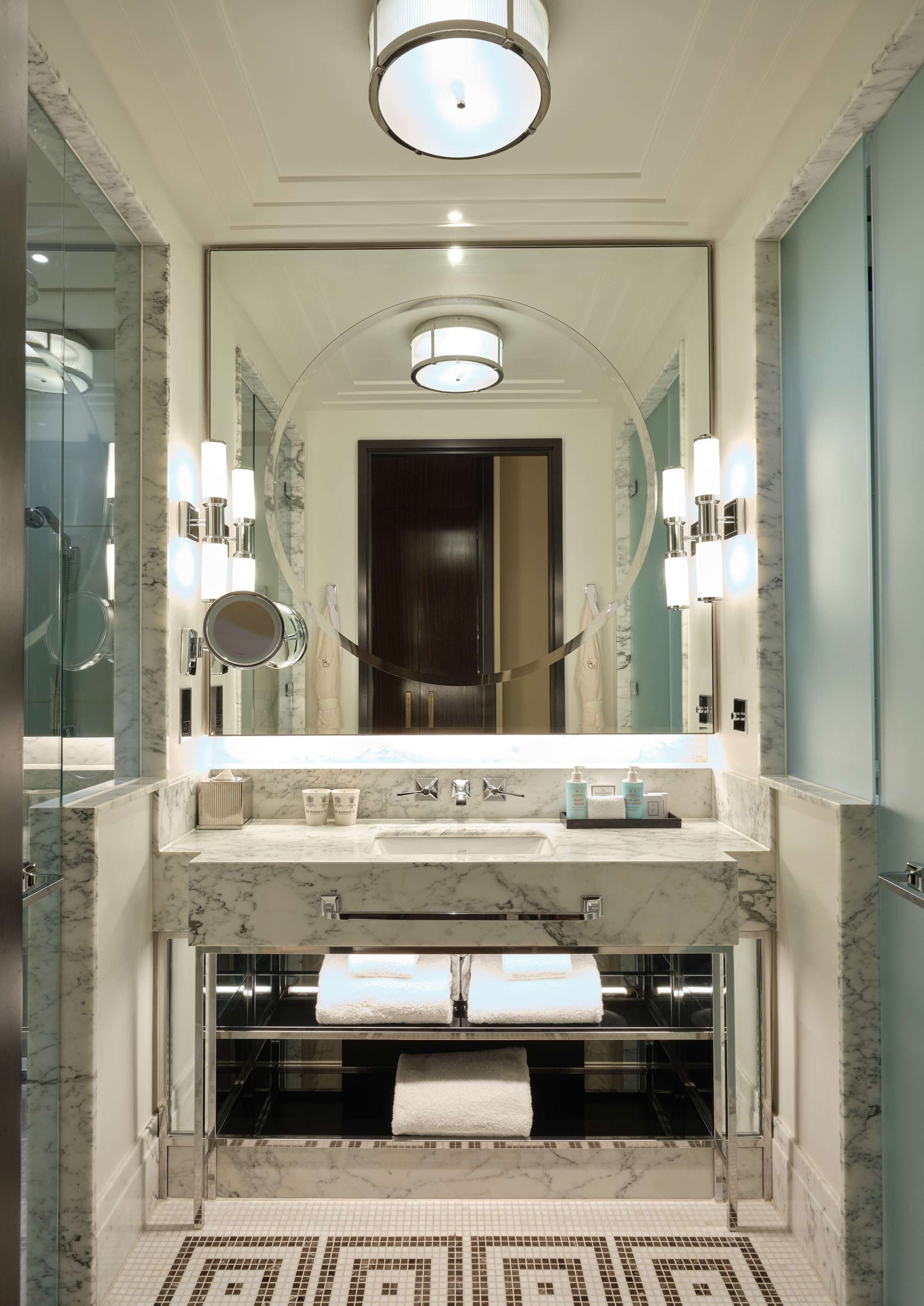 A modern bathroom with a large mirror, marble countertops, a built-in sink, and a towel rack.