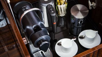 A compact coffee station with a coffee maker, a kettle, and a cup warmer, along with two white cups and saucers.