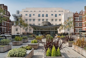 A hotel with a central courtyard featuring planters with various plants, a modern glass entrance, and a traditional building facade. - The Beaumont Mayfair (London)